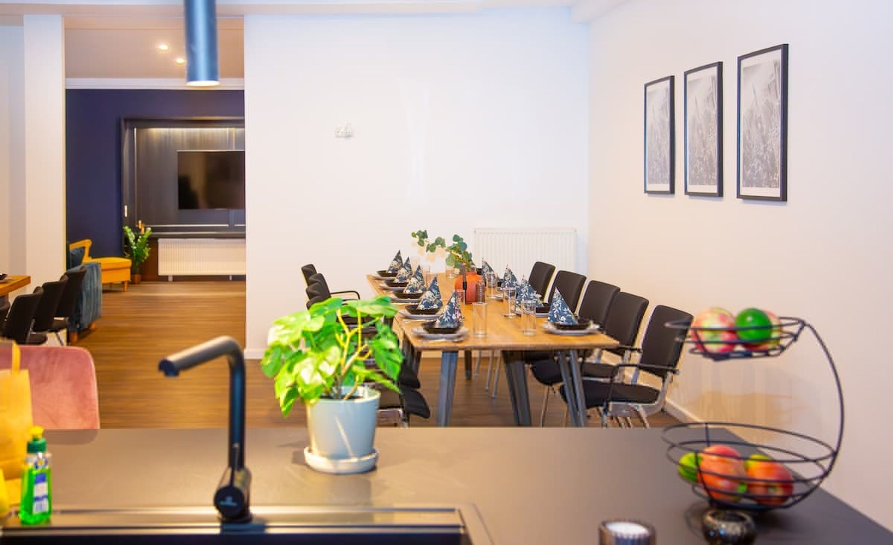 A modern conference room with a long table, chairs, potted plants, and framed pictures on the wall.