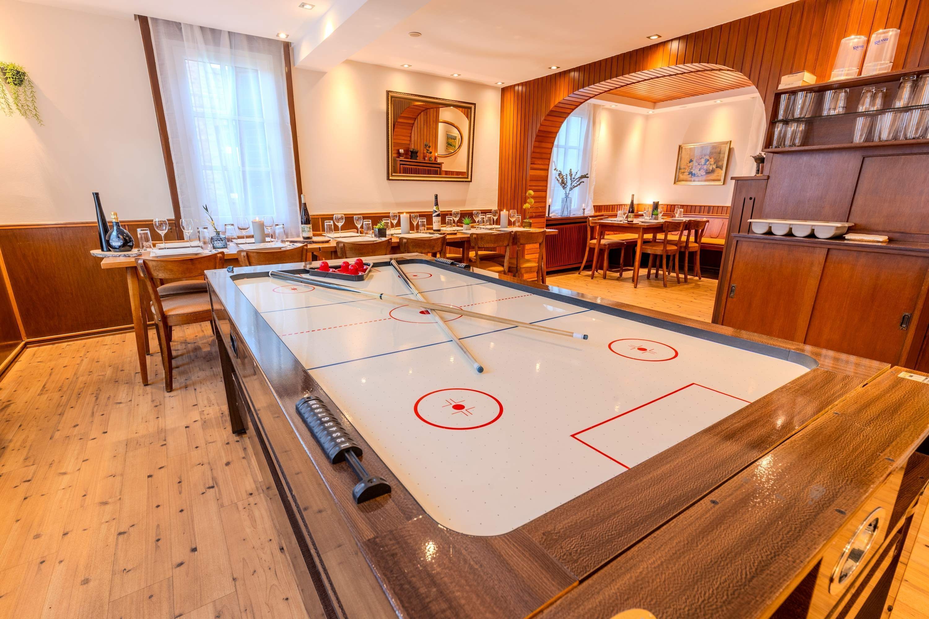 A room with a shuffleboard table, wooden furniture, and a dining area with tables and chairs.