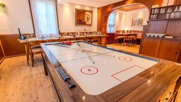 A room with a shuffleboard table, wooden furniture, and a dining area with tables and chairs.