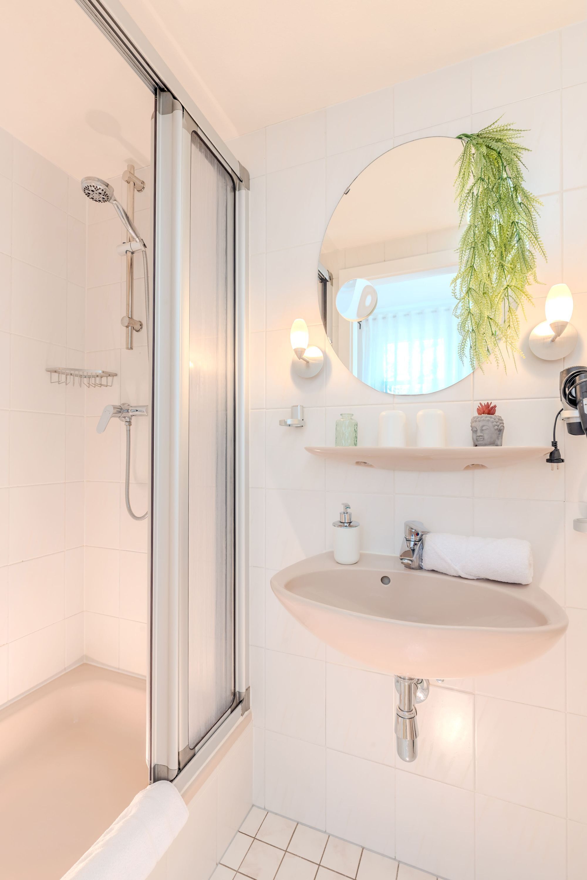 Ein Badezimmer mit einer Duschkabine, einem Waschbecken mit Spiegel darüber und einer Topfpflanze.