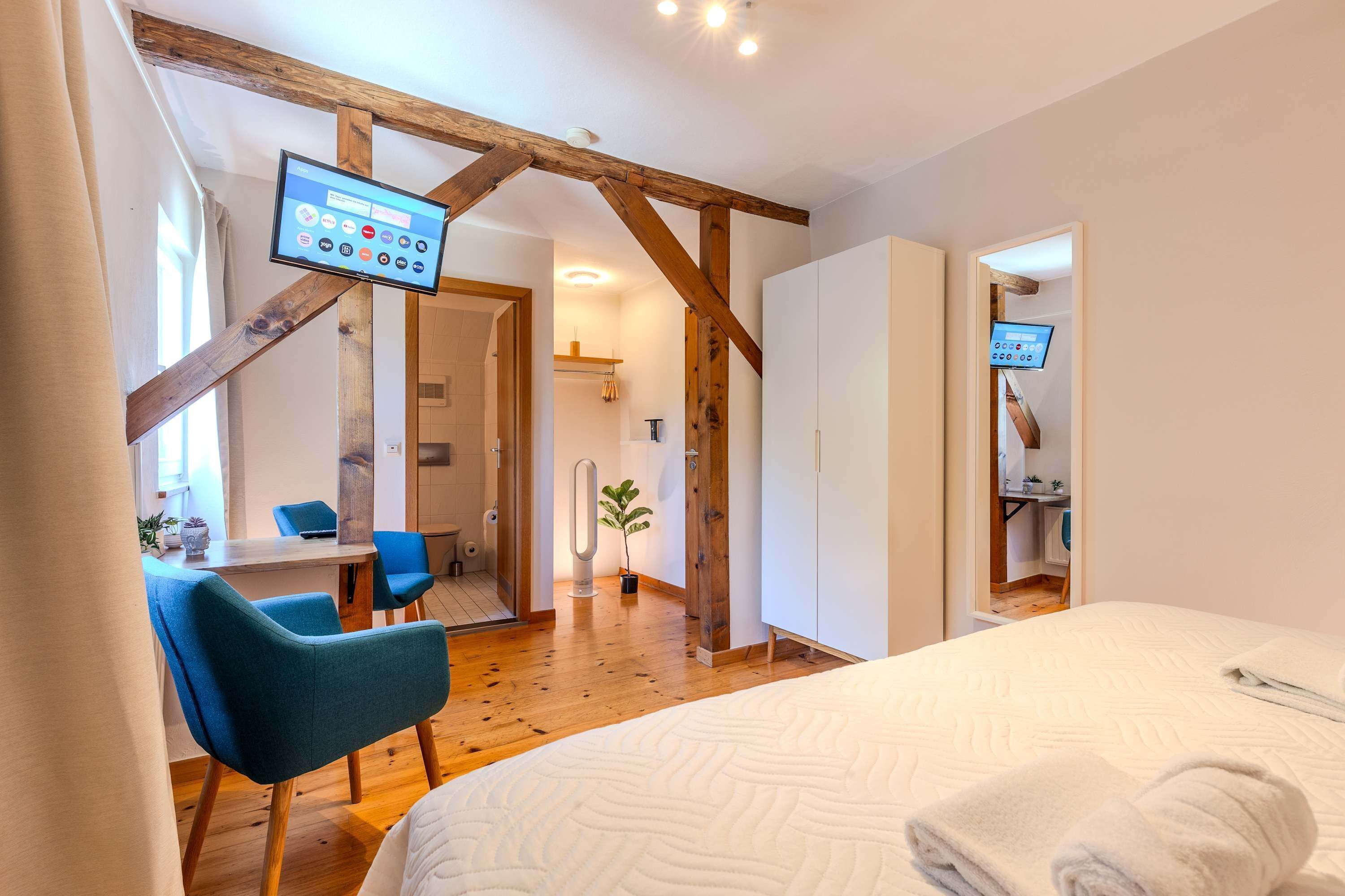 Une chambre d’hôtel équipée d’un lit, d’un bureau, d’une chaise et d’un téléviseur fixé sur une poutre en bois.