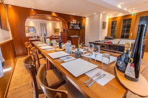A dining area with a long wooden table set for a meal, chairs, a pool table, and a bar area with bottles. - Weingut M Hlenschenke Game-room Vineyard and More (Sankt Goar)