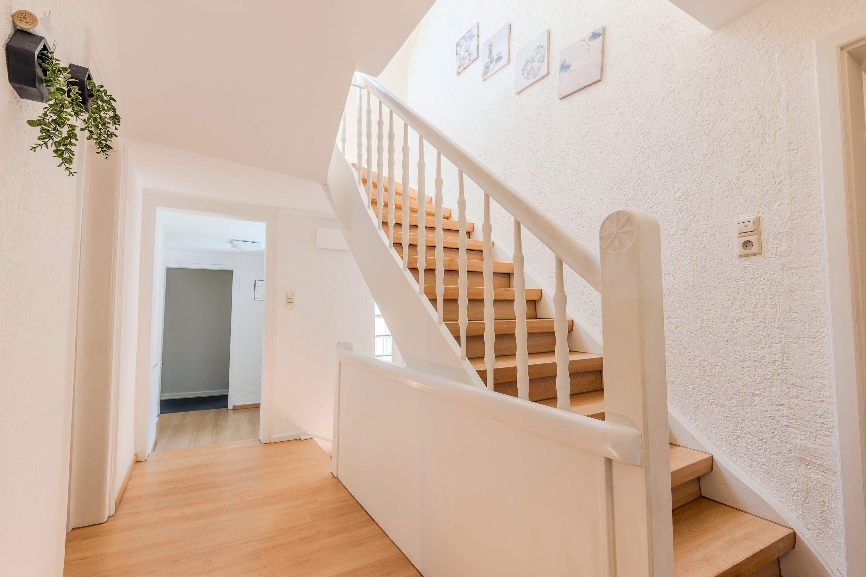 Eine Treppe mit Holzdielen und weißen Geländern, die zu einem Raum mit weißer Wand und einer Tür führt.