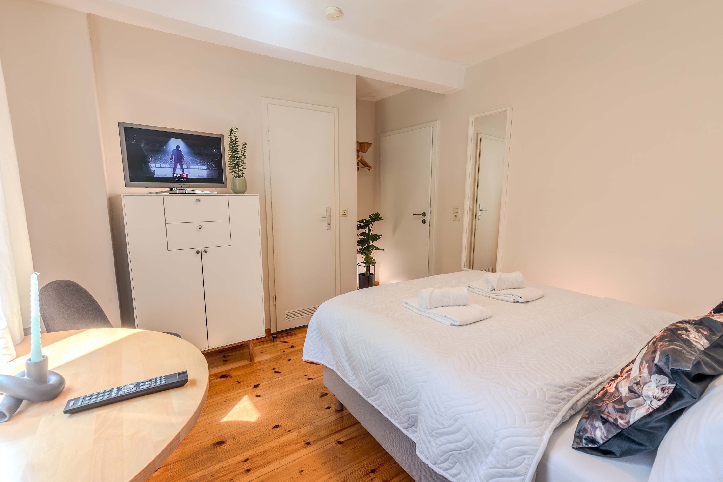 Ett hotellrum med en säng, en tv på ett stativ, ett skrivbord med en fjärrkontroll och en garderob.