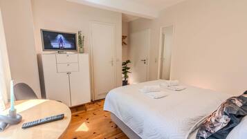 Ett hotellrum med en säng, en tv på ett stativ, ett skrivbord med en fjärrkontroll och en garderob.