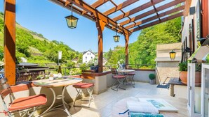 Un patio al aire libre con pérgola, mesas, sillas y vistas a una colina.
