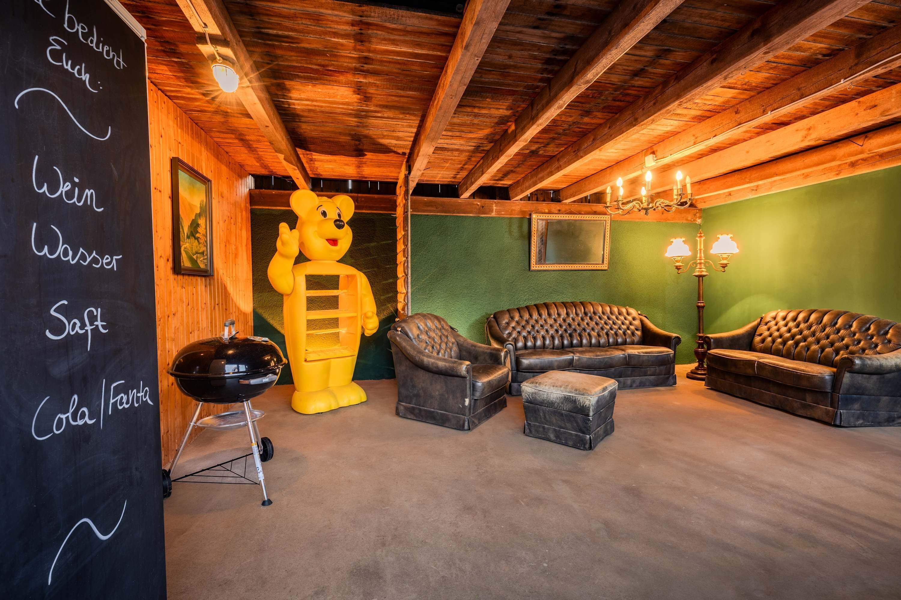Ein gemütlicher Raum mit Holzbalkendecke, einer großen Bärenstatue, Ledersofas und einer Tafel mit Speiseangeboten.