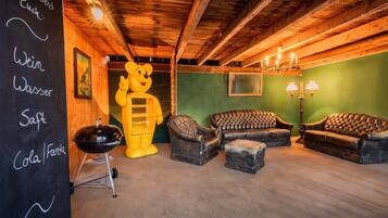 Ein gemütlicher Raum mit Holzbalkendecke, einer großen Bärenstatue, Ledersofas und einer Tafel mit Speiseangeboten.