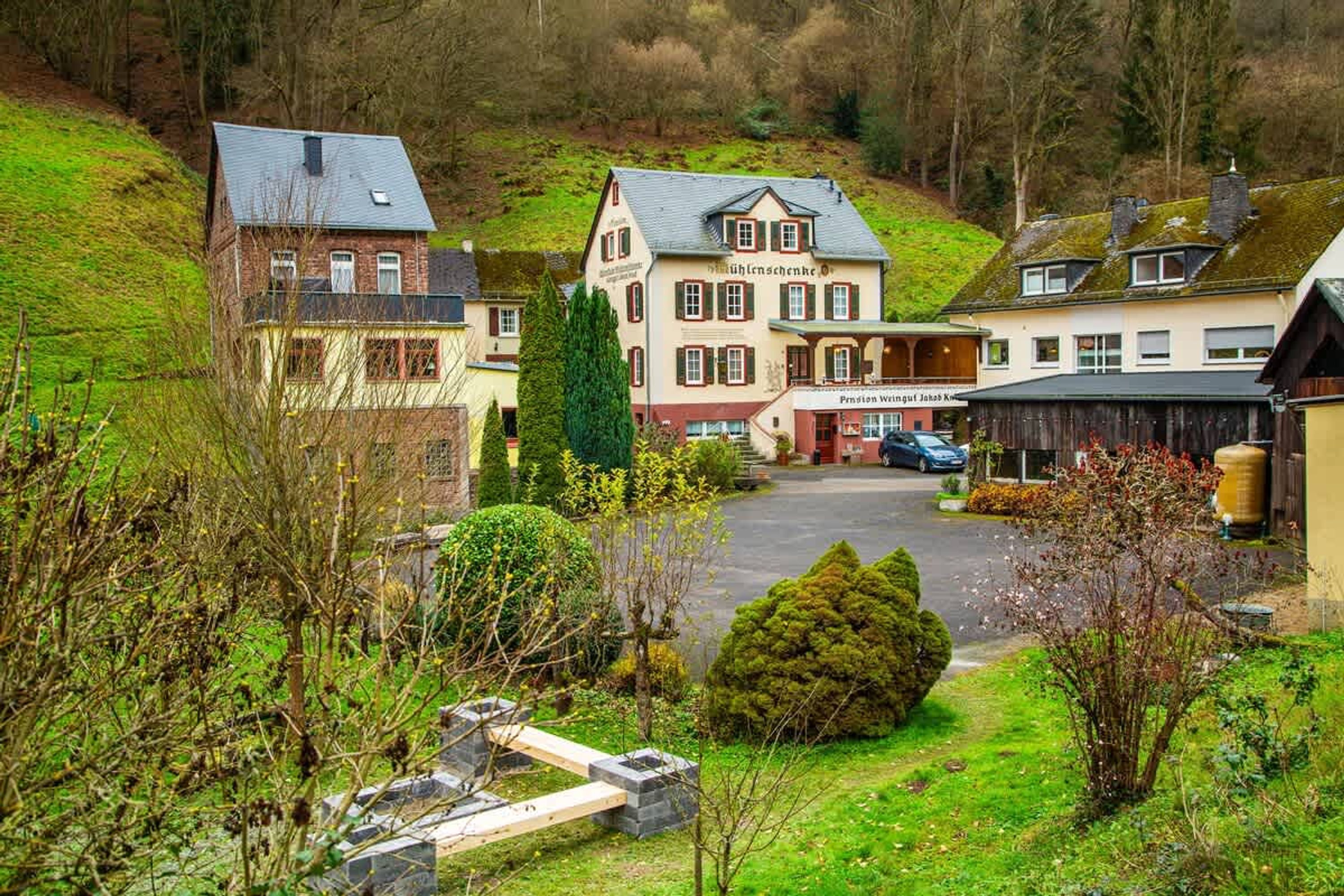 Ein traditionelles europäisches Gebäude mit einem zentralen Eingang, einem Parkplatz und einem Hang im Hintergrund.