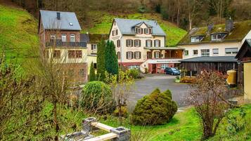 Ein traditionelles europäisches Gebäude mit einem zentralen Eingang, einem Parkplatz und einem Hang im Hintergrund.