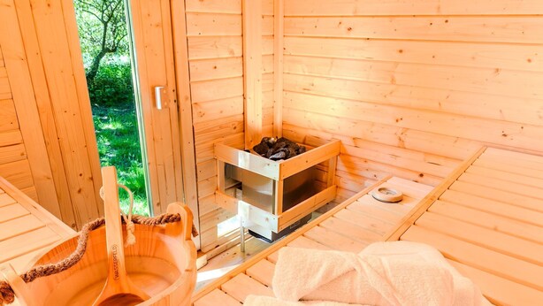 Un sauna de madera con un banco de madera, un tazón grande de madera y un estante con objetos.