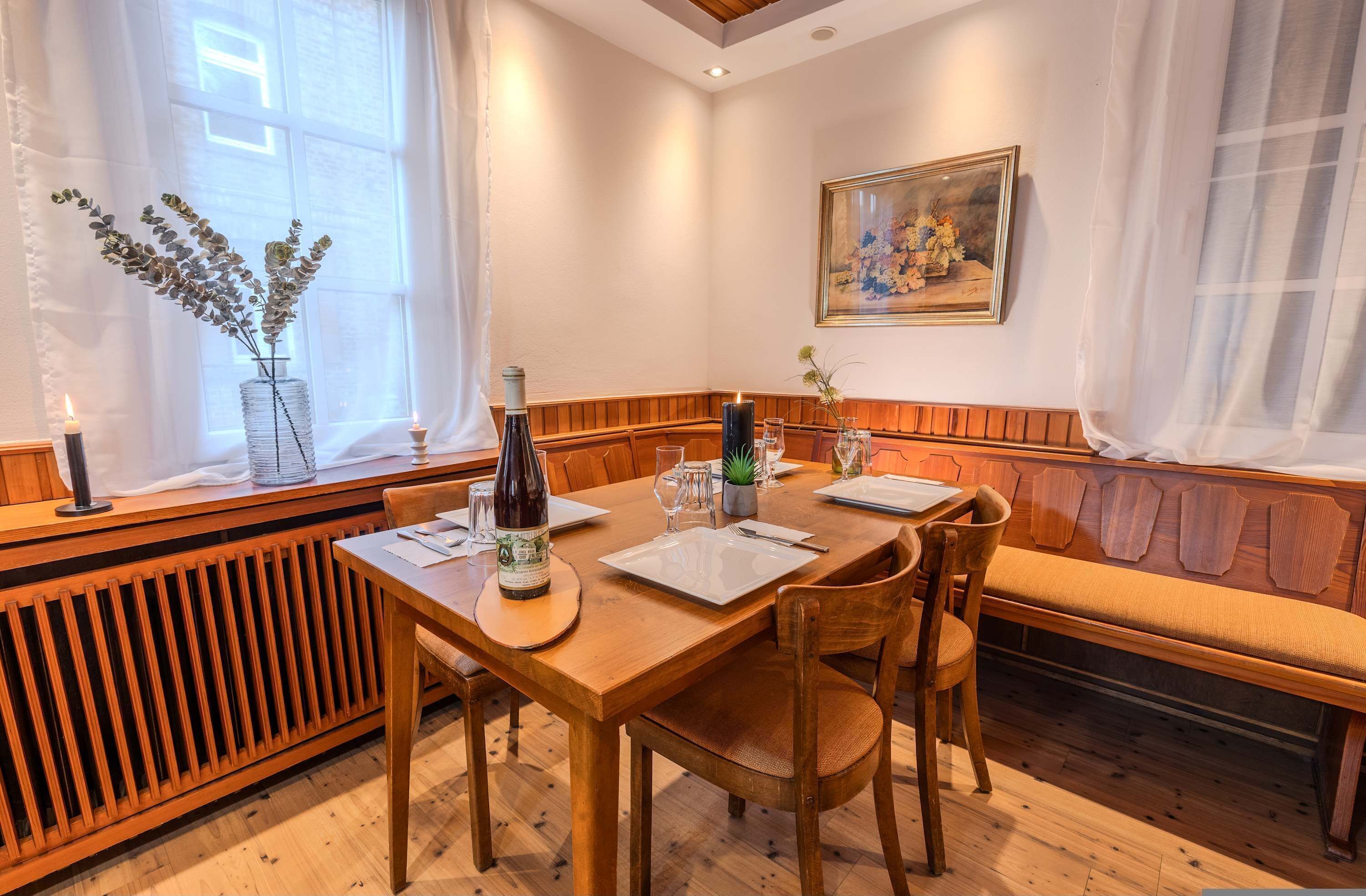 A dining area with a wooden table set for two, a bench, and a radiator.