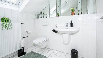 A modern bathroom with a skylight, white tiles, a toilet, a sink, and a trash bin.