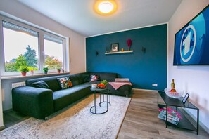 A modern living room with a dark green sofa, a small round table with a candle, and a magazine on a black side table.