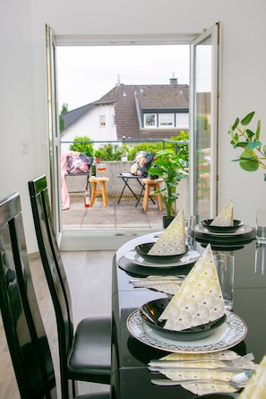 A dining area with a table set for two, a chair, and a view of the outside.