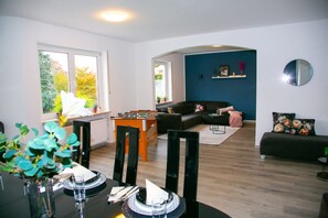 A modern living room with a dining table, chairs, a sofa, and a foosball table.