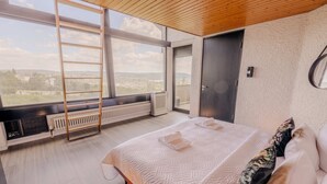 A bedroom with a large window, a ladder, a bed with pillows, and a radiator. - Villa Panoramica Pool Sauna (Weitersburg)
