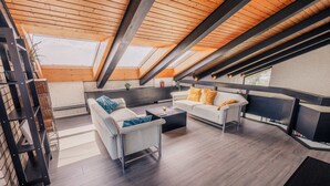 A modern loft-style room with a sloped ceiling, built-in shelves, a sofa set, and a dining area. - Villa Panoramica Pool Sauna (Weitersburg)