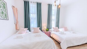 A hotel room with two beds, a small table, and a window with curtains. - Villa Bueckeberg Game-room and Wellness (Luhden)