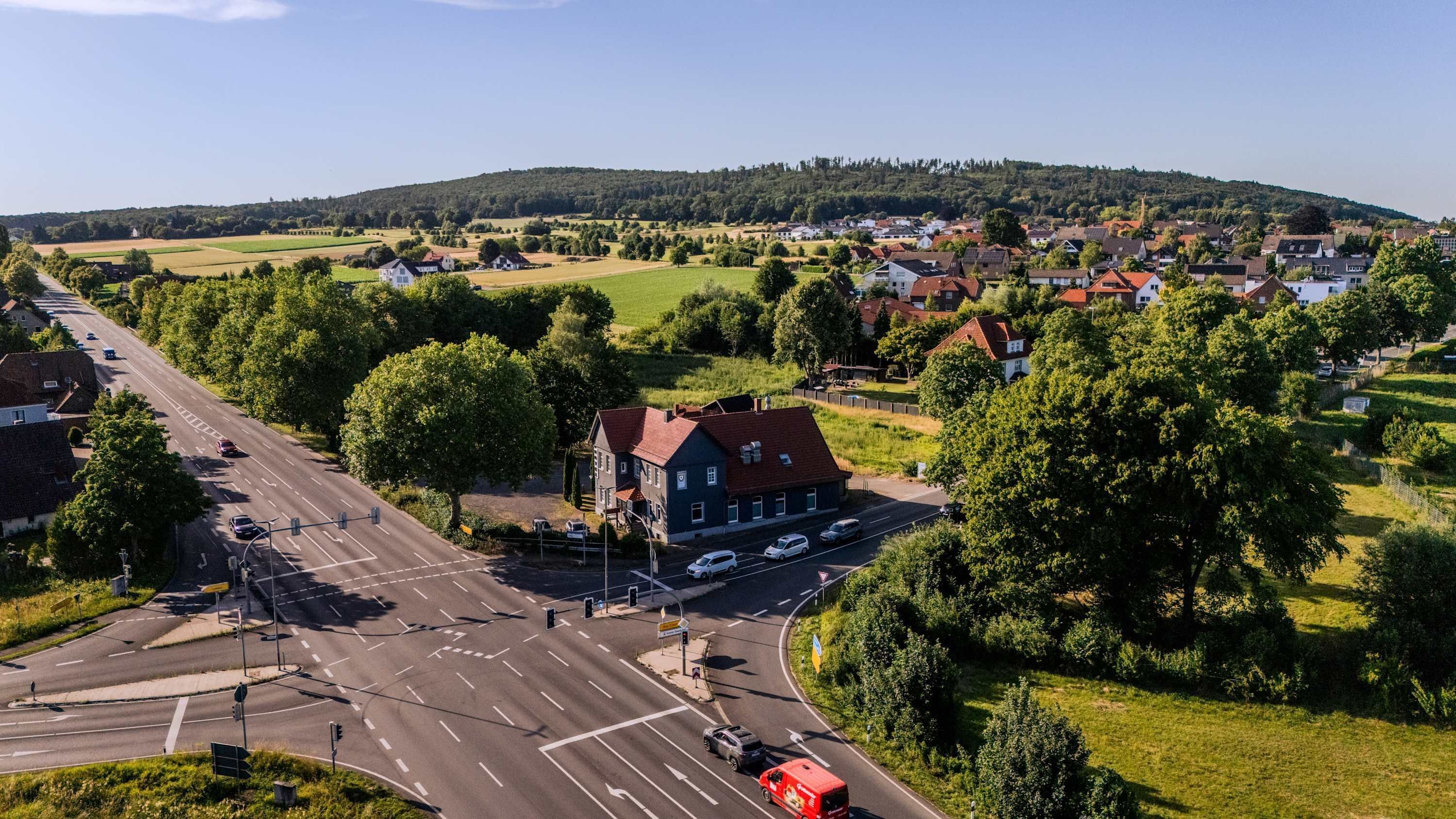 An aerial view of a town with a main road, residential houses, and a hill in the background.