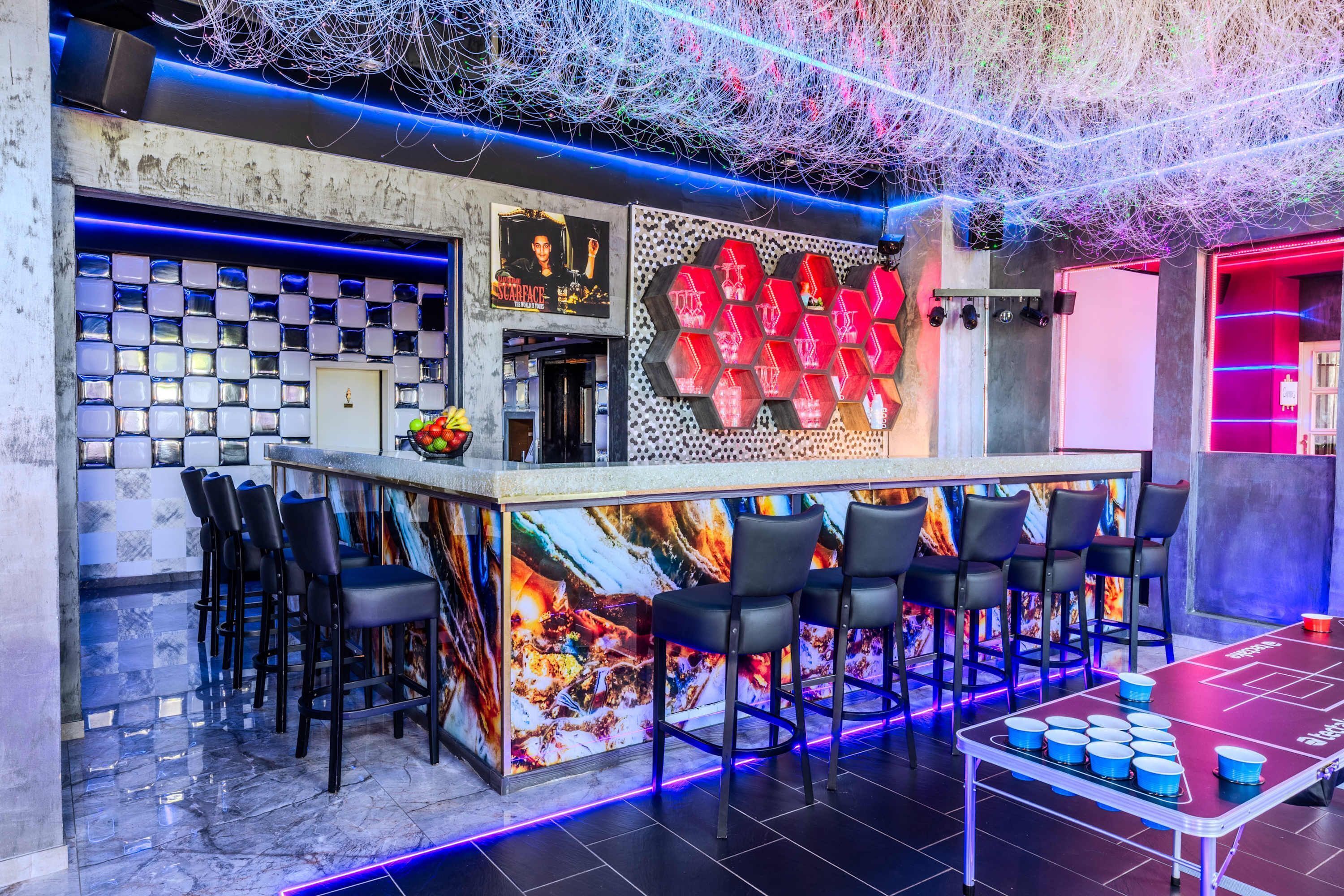 Un espace bar avec un sol à carreaux, des tabourets de bar, un plafond éclairé par des néons et une enseigne lumineuse au néon.