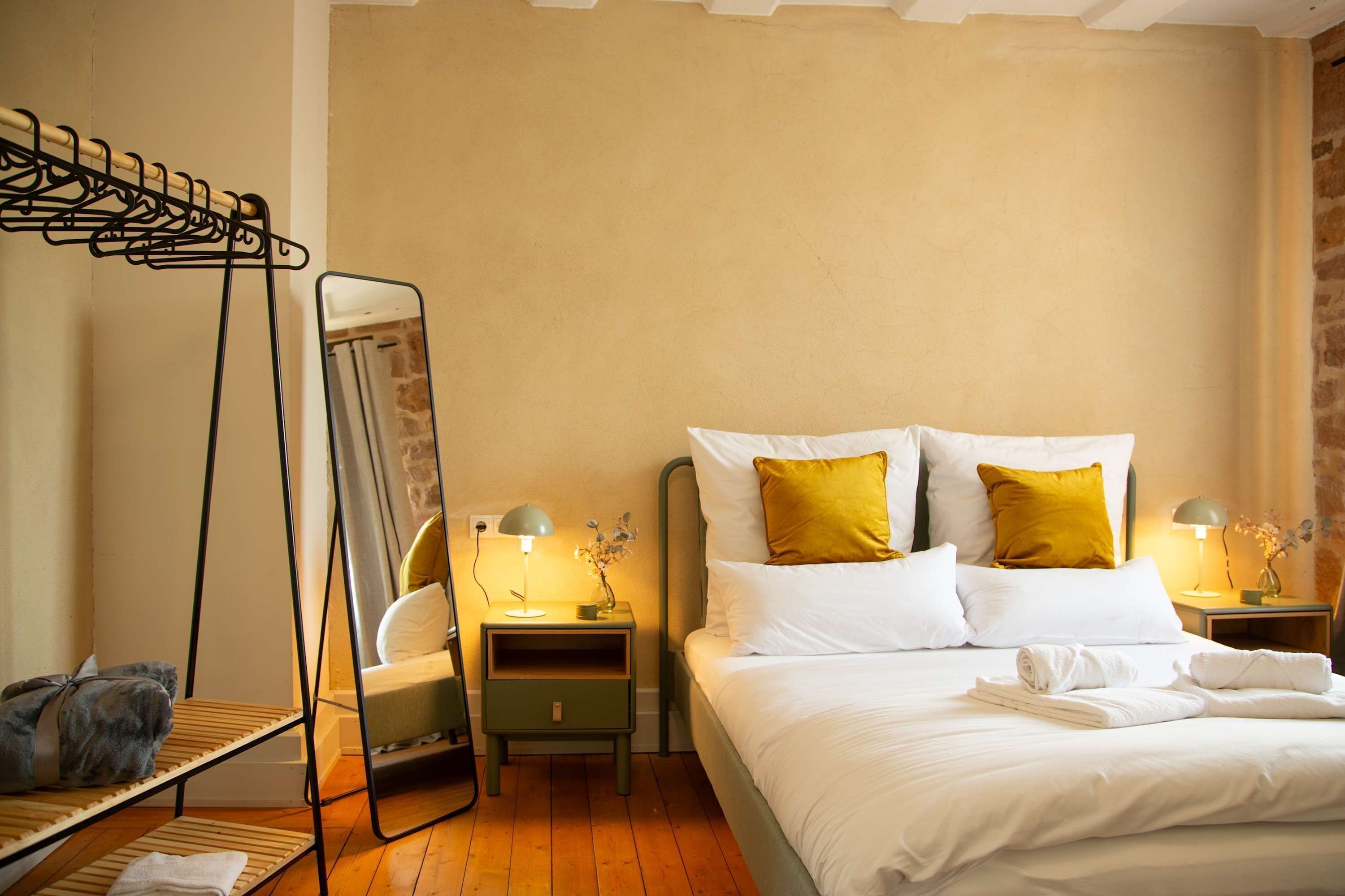 Quarto com uma cama, duas mesas de cabeceira, um cabideiro e um espelho.