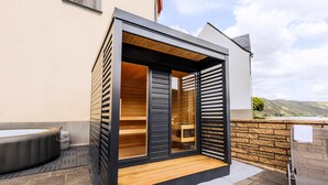 A modern outdoor sauna with a wooden deck, a hot tub, and a stone wall. - Whirlpool Sauna Kino Villa Klosterschenke (Sankt Goarshausen)