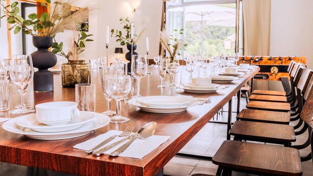 A dining table set with plates, glasses, and cutlery, flanked by chairs and a view of the outdoors. - Whirlpool Sauna Kino Villa Klosterschenke (Sankt Goarshausen)
