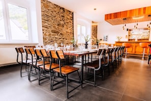 A dining area with a stone wall, wooden chairs, and a bar counter. - Whirlpool Sauna Kino Villa Klosterschenke (Sankt Goarshausen)