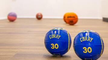 Two basketballs with the name 'Curry' and the number '30' on a wooden floor, with a basketball hoop and an NBA logo in the background.