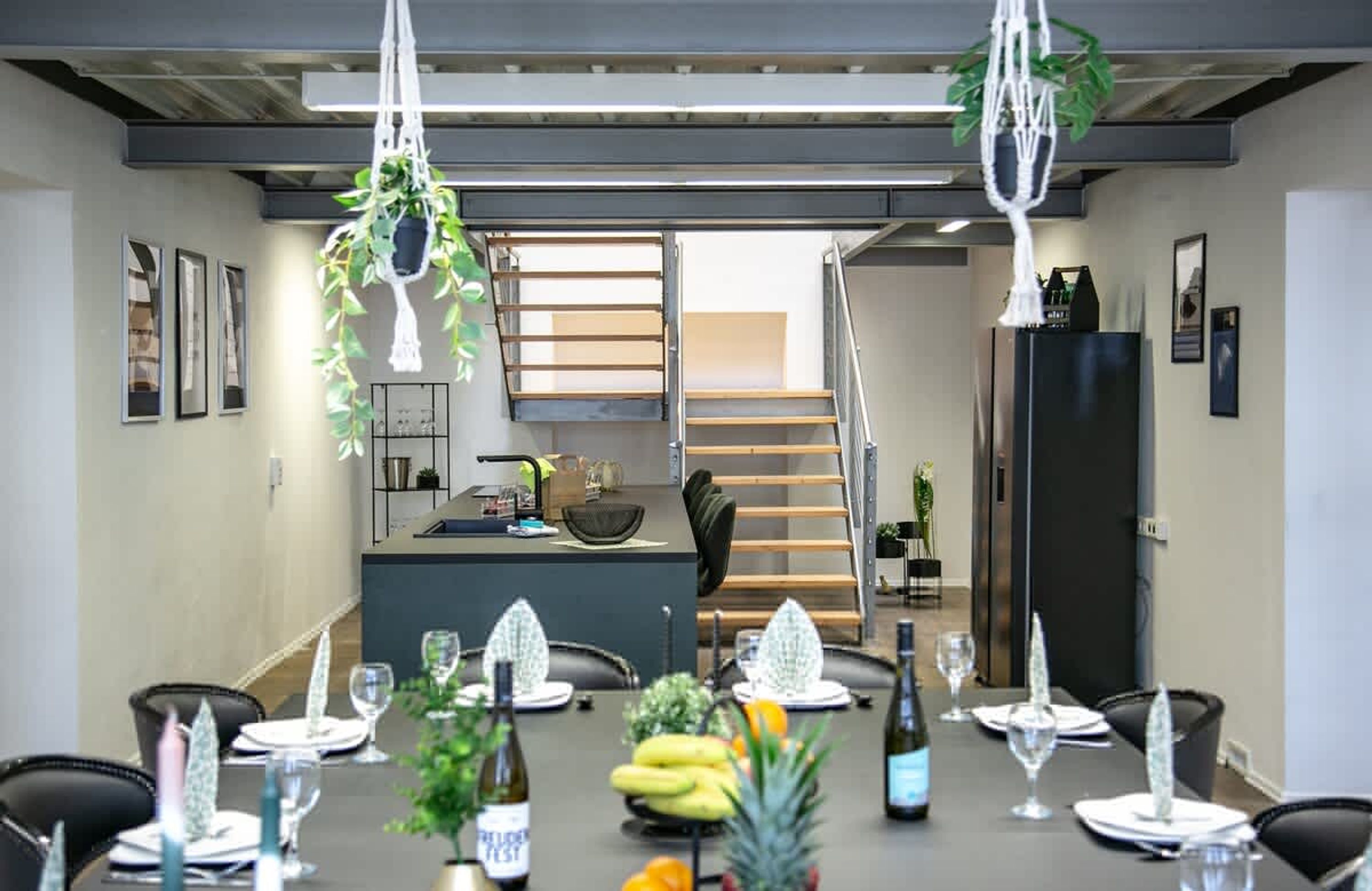 A dining area with a long table set for a meal, a staircase, and a kitchen area in the background.