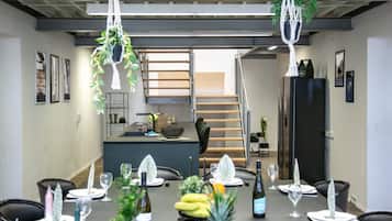 A dining area with a long table set for a meal, a staircase, and a kitchen area in the background.