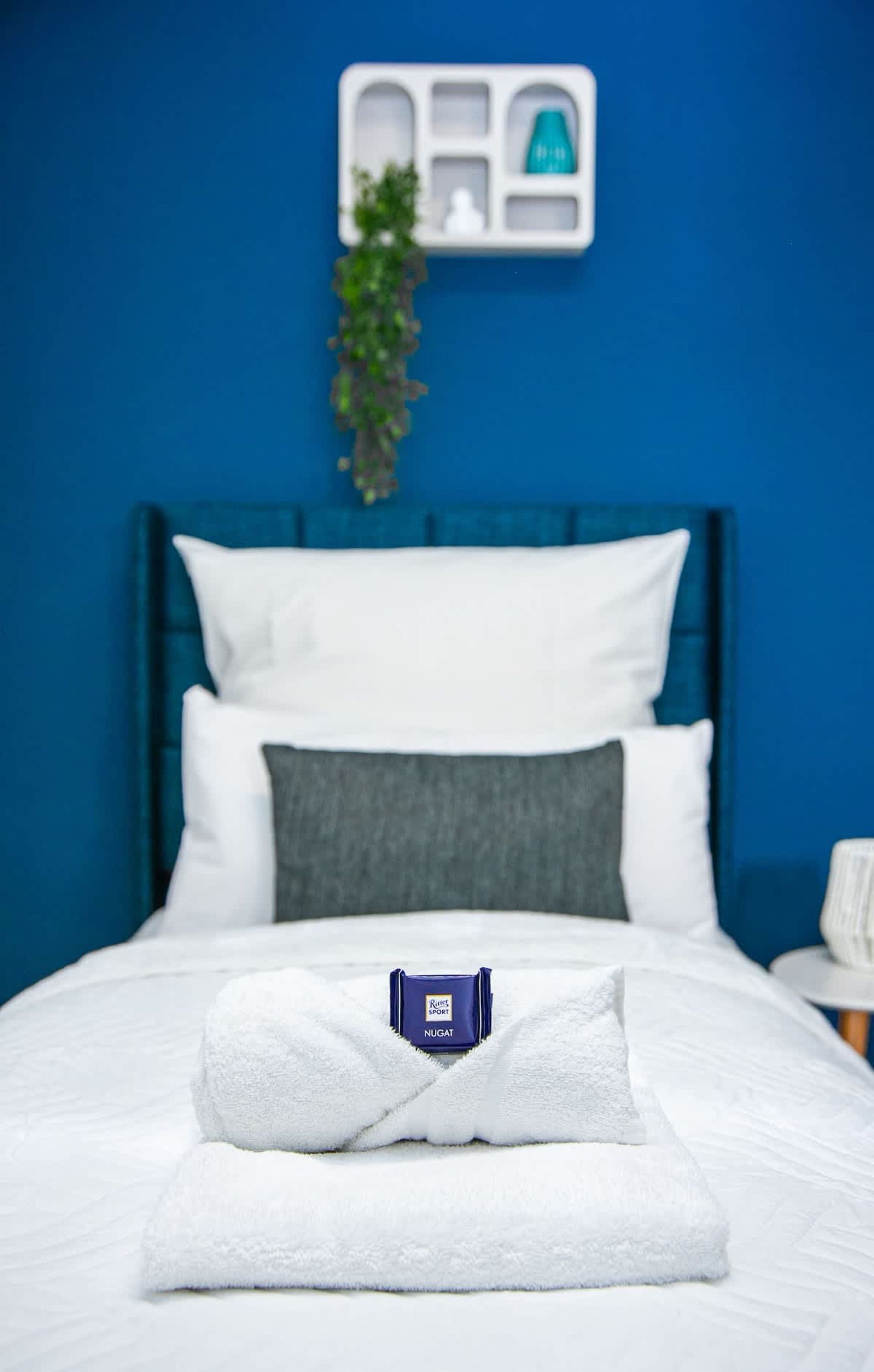A neatly made bed with a folded white towel and a NUGAT branded item on it.