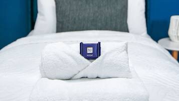 A neatly made bed with a folded white towel and a NUGAT branded item on it.