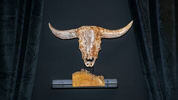A mounted bull skull with horns, mounted on a wooden base, against a dark background.