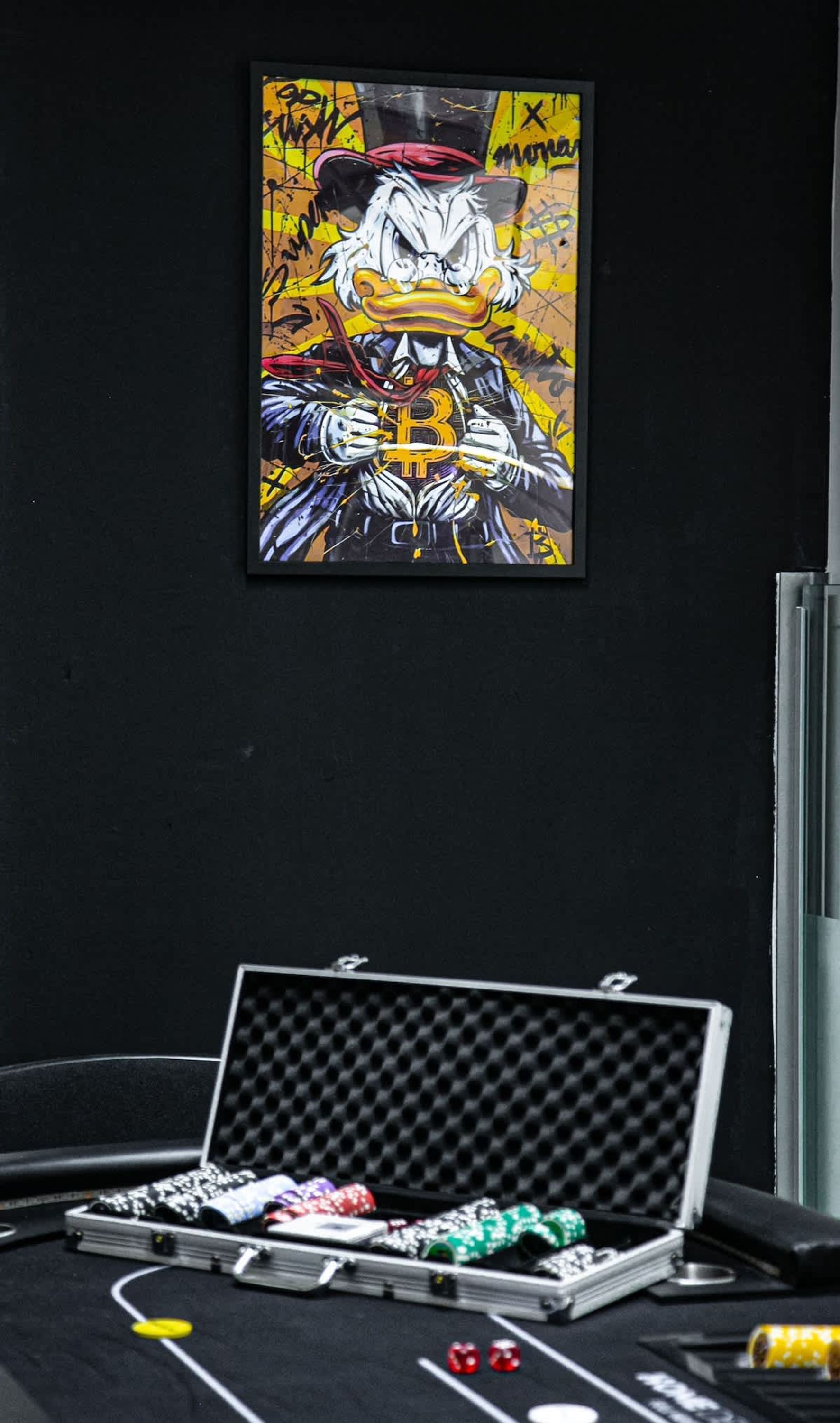 A framed artwork of a cartoon character holding a Bitcoin symbol, a poker table with chips and dice, and a black wall.