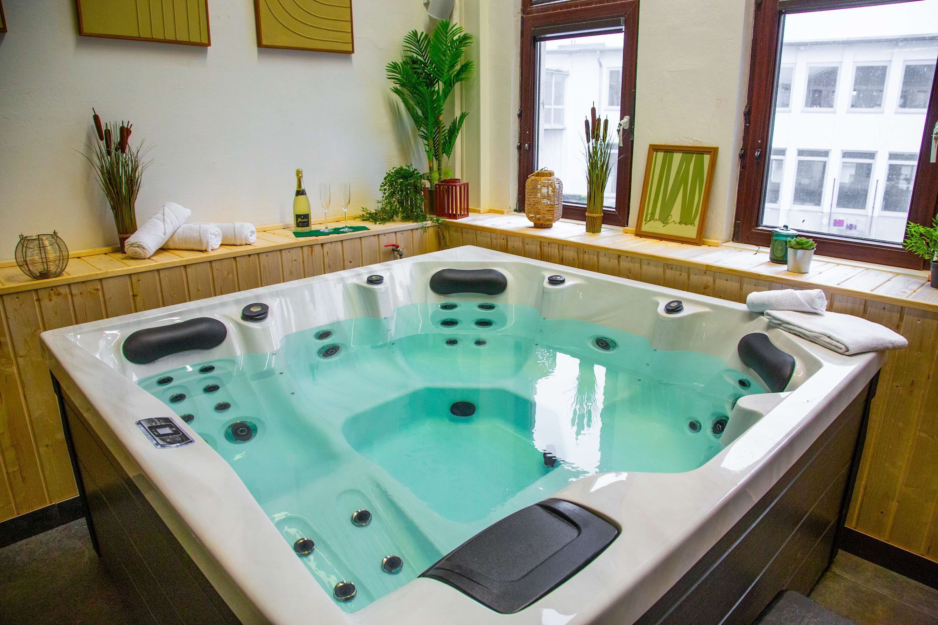 Une salle de spa dotée d’un grand jacuzzi, de lambris en bois et de différentes plantes disposées sur le rebord de la fenêtre.
