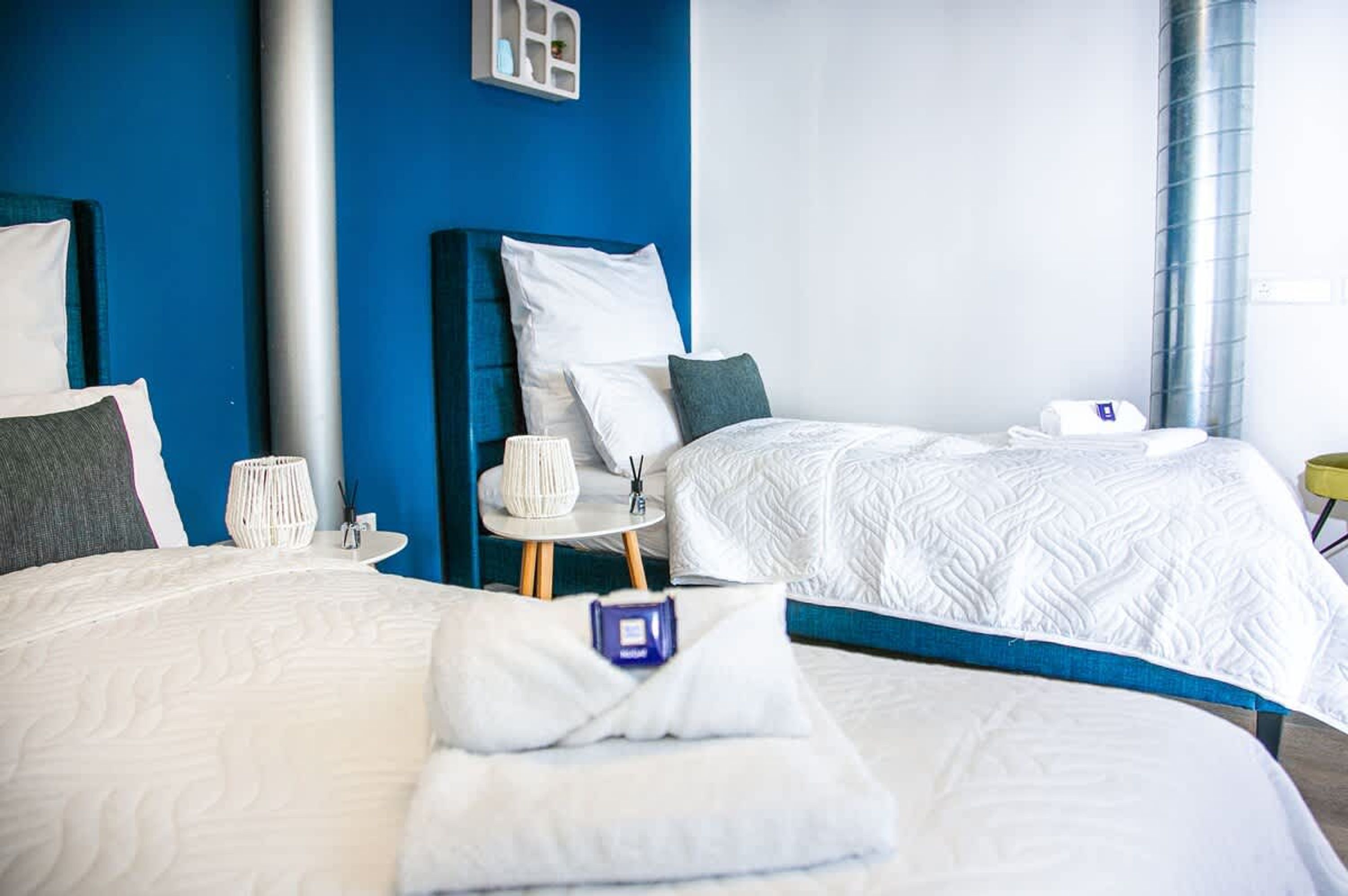 A hotel room with two beds, a small table, and a wall unit with a shelf.
