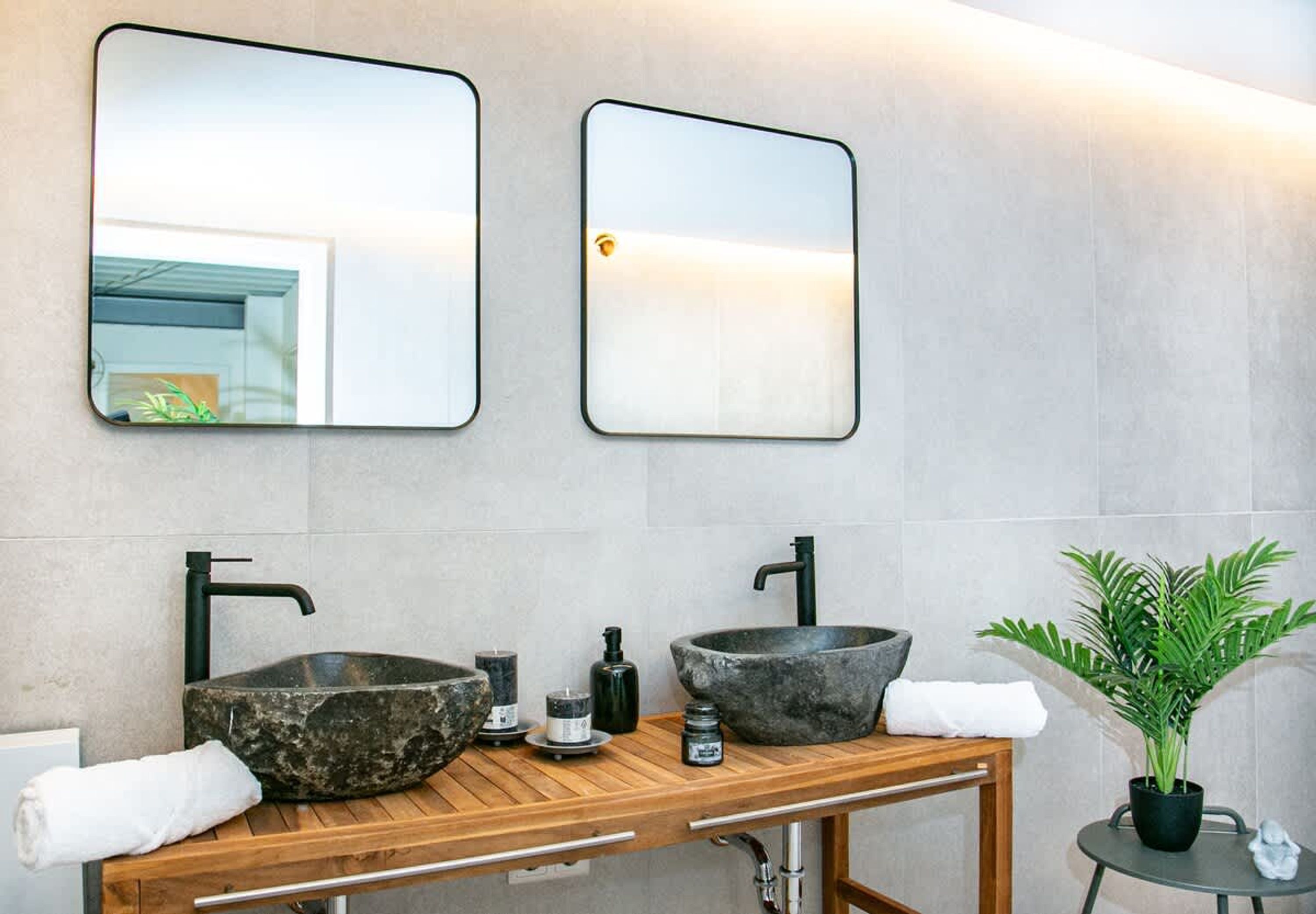 Een badkamer met twee stenen wastafels, een houten wastafelmeubel en twee spiegels aan de muur.