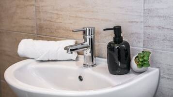 Een wastafel met een chromen kraan, een zwarte zeepdispenser en een witte handdoek.