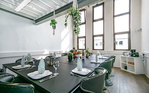 A dining area with a long table set for a meal, chairs, hanging plants, and large windows. - Casino Whirlpool-sauna-kino-indoor-basketball (Hoehr-Grenzhausen)