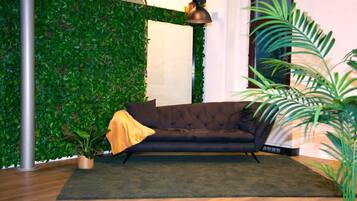 A room with a green wall, a dark sofa, a lamp, and a potted plant.