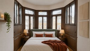A bedroom with a large bed, wooden paneling, two bedside tables with lamps, a plant, and large windows. - Besto Residence Kino-billard-poker-kicker (Albstadt)