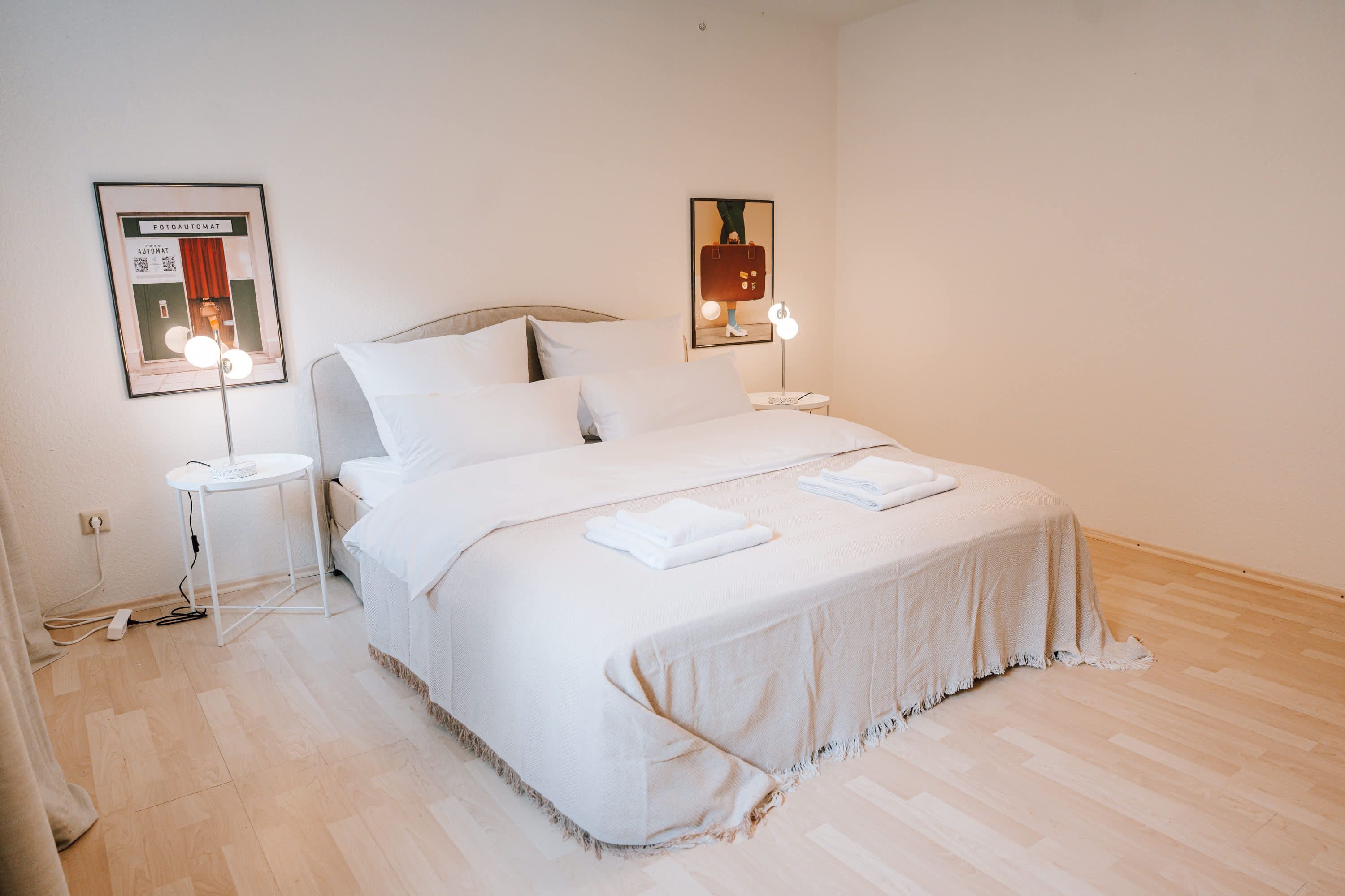 A neatly made bed with white linens, a bedside table with a lamp, and two framed pictures on the wall.