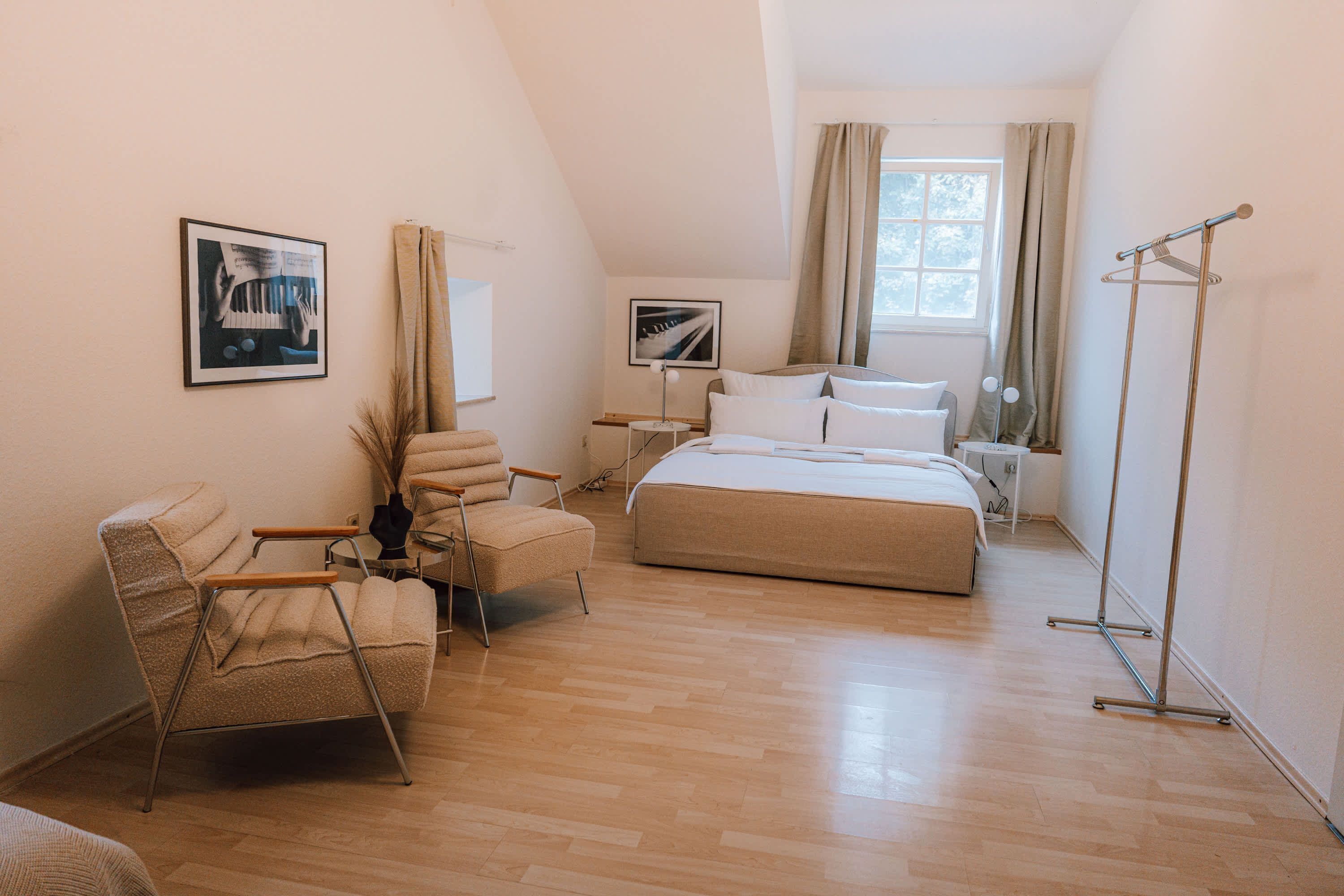 Un dormitorio con una cama, una silla, una mesita de noche, una lámpara de pie y una ventana con cortinas.