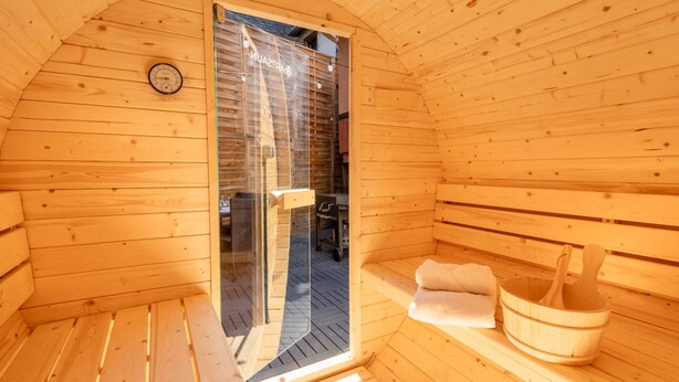 Un cuarto de sauna con paredes de madera, un banco, una toalla y un balde de madera.