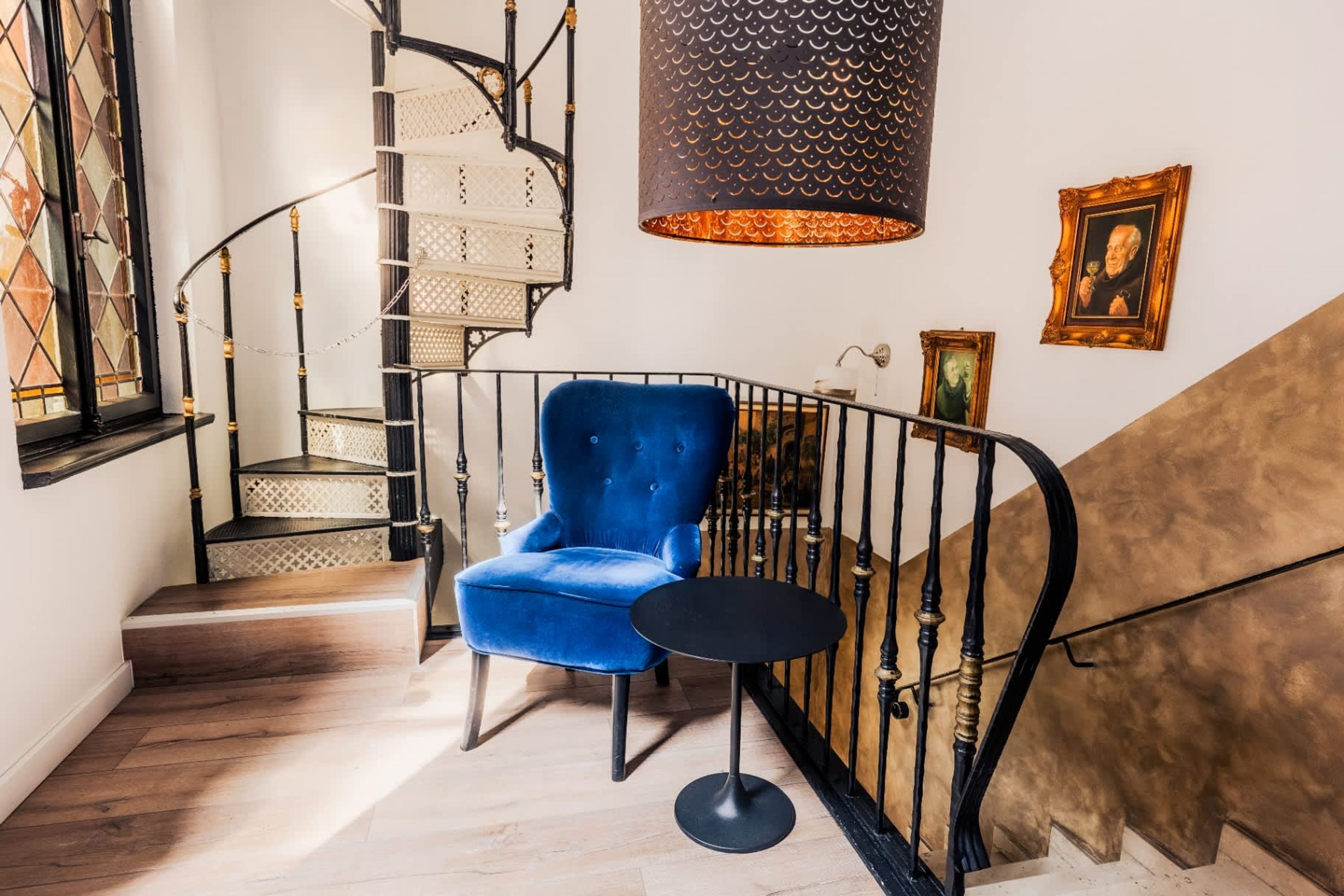 A staircase with a blue chair and a small table, a decorative wall hanging, and a patterned lamp.