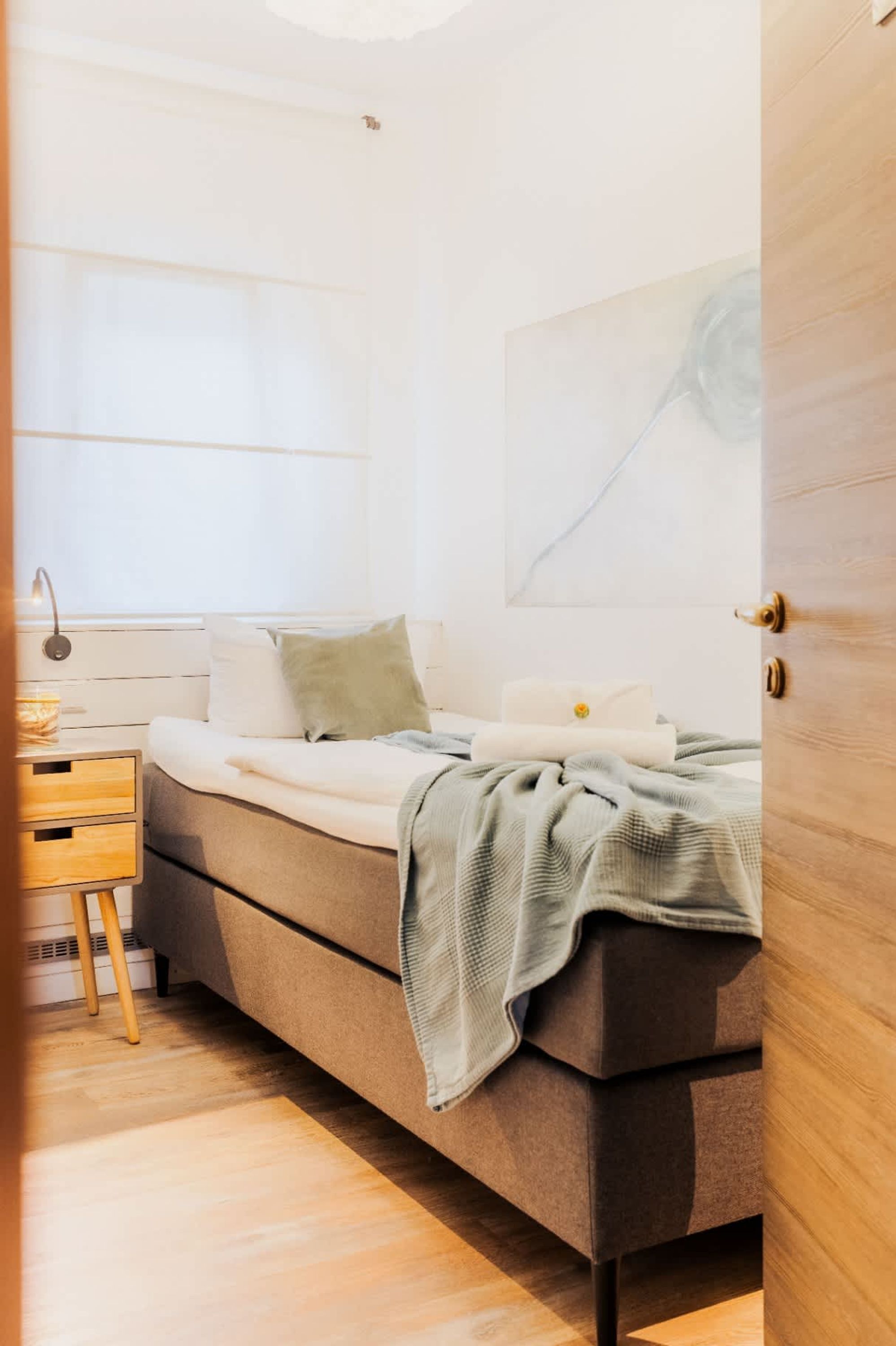 Un dormitorio con cama, mesita de noche, lámpara y un cuadro en la pared.