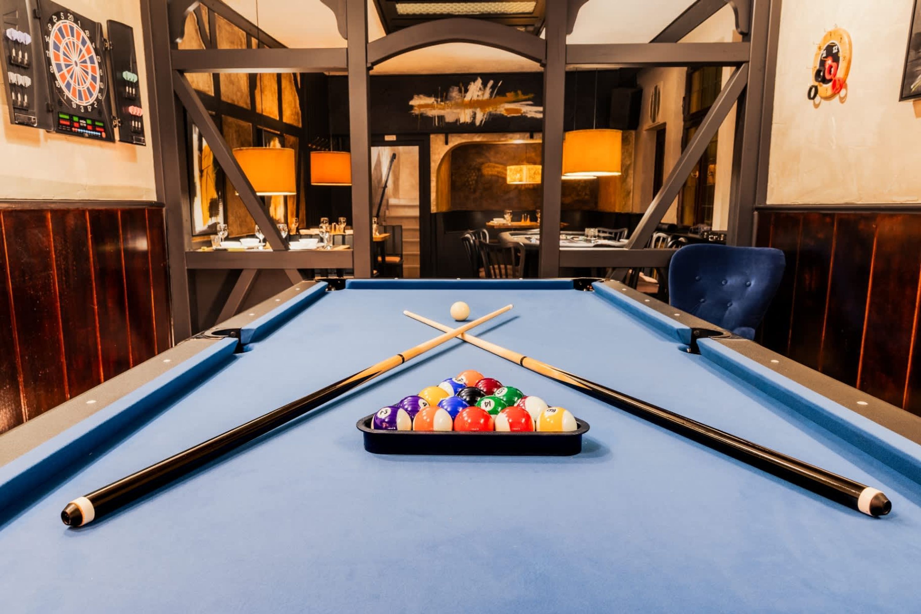 A pool table with balls and cues, a dartboard, and a bar area with seating.