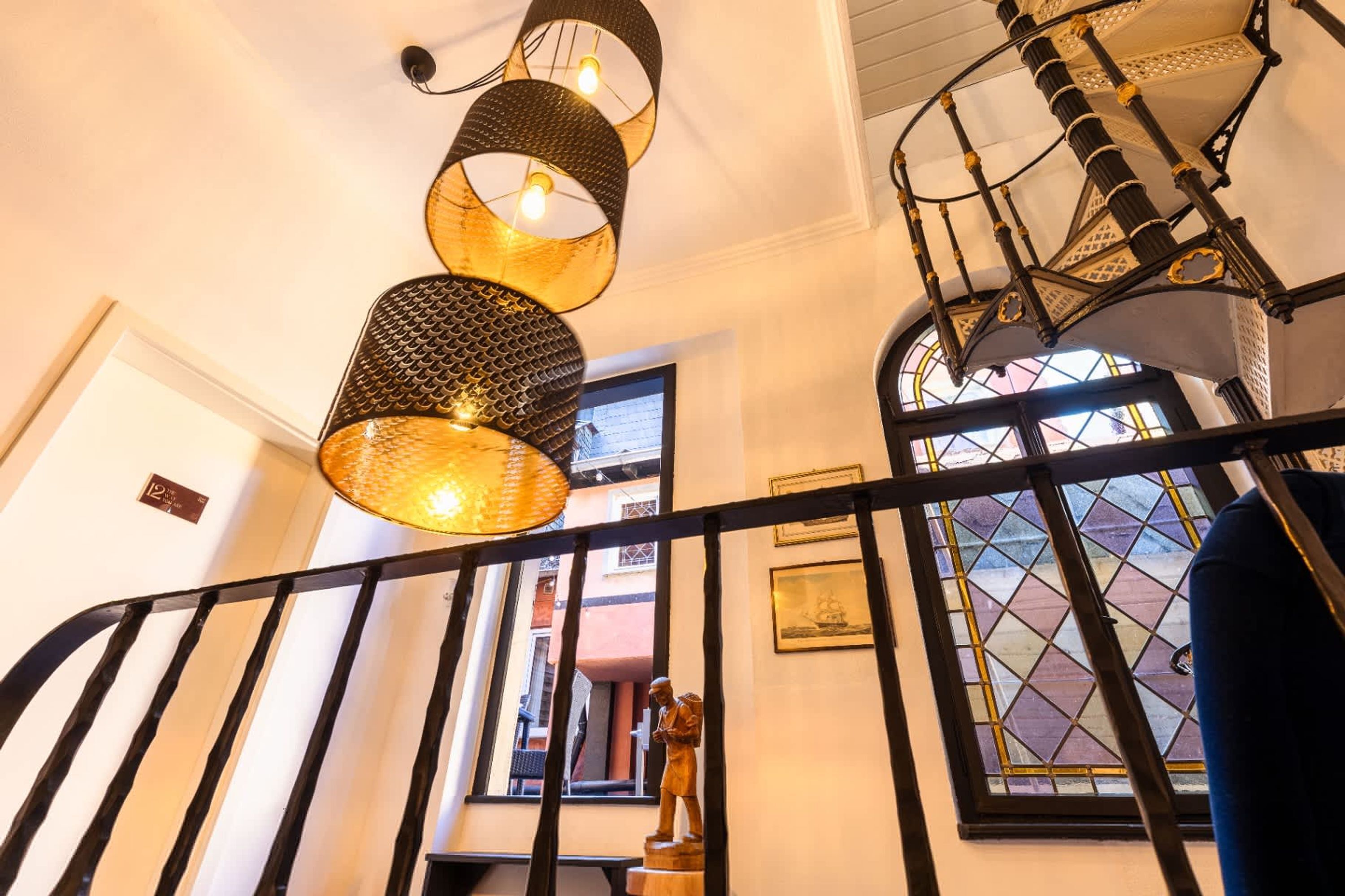 A staircase with a black railing, a wooden statue, and a window with a diamond pattern.